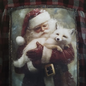May include: A red and black plaid flannel shirt with a framed image of Santa Claus holding a white fox. Santa is wearing a red hat and coat with white trim. The fox has white fur and a black nose.