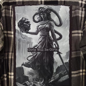 May include: A gray and black plaid flannel shirt with a large graphic on the back. The graphic is a black and white illustration of a woman holding a severed head and a sword, with the text "Girls Will Be Girls."