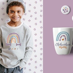 May include: A child wearing a striped long-sleeve shirt with a rainbow graphic and the word "Woof". A white mug with a rainbow design and the text "Chihuahua mom" is next to two round pins.