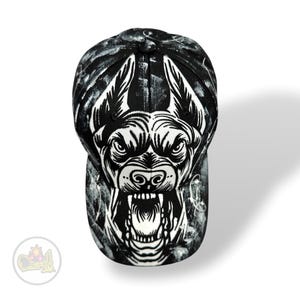 Puede incluir: Gorra de béisbol en blanco y negro con un llamativo gráfico de la cara de un perro gruñendo. La gorra tiene una visera curva y un patrón abstracto texturizado. El diseño es audaz y adecuado para ropa informal.