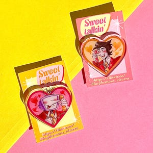 Puede incluir: Dos pines acrílicos en forma de corazón con personajes de dibujos animados y el texto "Sweet talkin'". Un pin presenta un personaje con cabeza de TV, el otro un hombre. Ambos pines tienen el sitio web linktr.ee/Blasphemous_viscera.