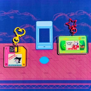 May include: Three colorful keychains with pixelated designs. One is a yellow floppy disk with the text "SPAMTON" and "LOVE-LETTER-FOR-YOU TXT VHS". Another is a green VHS tape with "STARRING MR ANT TENNA" and "WORTH SEEING!". The third is a light blue pixelated rectangle.