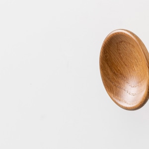 Puede incluir: Un pomo de armario de madera con un diseño redondeado en forma de cuenco. El pomo está hecho de madera marrón claro y tiene un pequeño vástago cilíndrico.