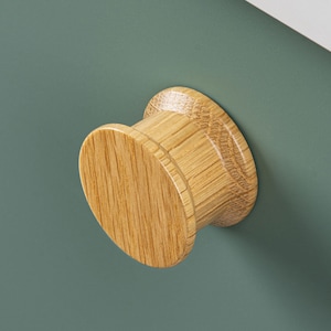 Peut inclure: Un bouton rond en bois avec une finition brun clair. Le bouton est fixé à une surface verte.