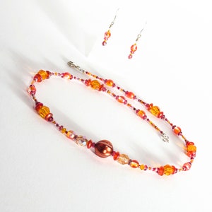 May include: A necklace and earrings set with orange, red, and clear glass beads. The necklace features a large, round, copper-colored bead.