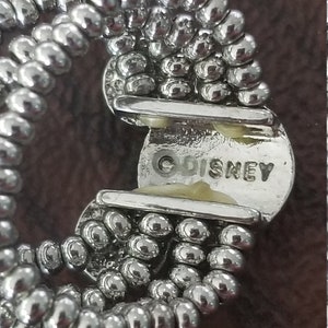 May include: Close-up of a silver-toned bracelet with a beaded design. The bracelet has a clasp with the word "DISNEY" stamped on it. The beads are small and round, and the bracelet appears to be vintage.
