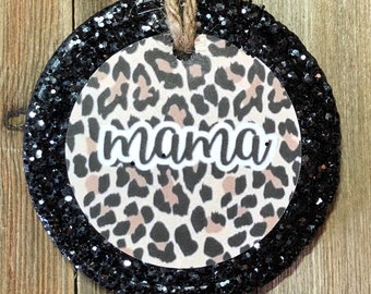 May include: A round, black glitter ornament with a white and brown leopard print design and the word "mama" in white script.