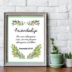 Könnte beinhalten: Ein gerahmter Druck mit grünem Hintergrund und weißem Rahmen. Der Druck zeigt eine Aquarell-Illustration von Olivenzweigen mit gelben Oliven. Der Text "Friendship" ist in schwarzer Kursivschrift geschrieben. Unter der Illustration steht der Text "As iron sharpens iron, so one person sharpens another" in schwarzer Schrift. Der Text "Proverbs 27:17" steht in schwarzer Schrift unter dem Zitat.