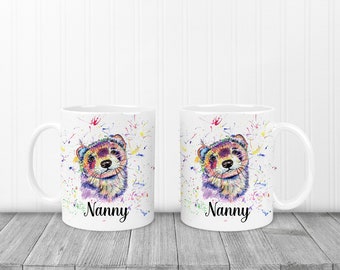 May include: Two white ceramic mugs with a colorful watercolor illustration of a ferret's face. The mugs have the word "Nanny" printed on the bottom in black.