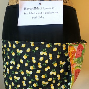 May include: Reversible apron with black fabric and a lemon print on one side and a fruit print on the other. The apron has the text "Reversible 2 Aprons in 1 Fun Fabrics and 3 pockets on Both Sides".