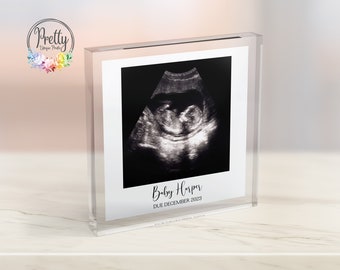 May include: A clear acrylic block displaying a black and white ultrasound image. The image shows a baby. The text "Baby Harper DUE DECEMBER 2023" is printed below the image. The block is on a white surface.