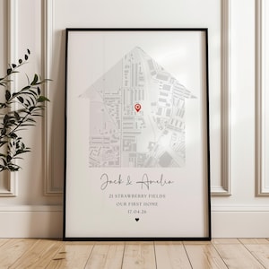 May include: A framed wall art print featuring a gray street map shaped like a house silhouette with a red location pin. Below the map, the text reads Jack & Amelia, 21 Strawberry Fields, OUR FIRST HOME, 17.04.26, and a small black heart icon.