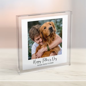 Puede incluir: Un bloque de foto de acr&iacute;lico transparente con una imagen de un hombre abrazando a un golden retriever. El texto "Happy Father's Day Woof from Tucker" est&aacute; impreso debajo de la foto.