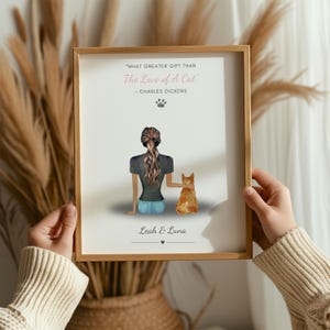May include: A framed print featuring an illustration of a person and a cat. The person is seated, facing away, with the cat beside them. The print includes the quote "WHAT GREATER GIFT THAN The Love of A Cat" by Charles Dickens, and the names "Leah & Luna".