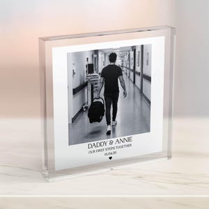 Puede incluir: Impresi&oacute;n fotogr&aacute;fica en blanco y negro en un bloque acr&iacute;lico transparente. La foto muestra a una persona caminando por un pasillo con un portabeb&eacute;s. El texto en la parte inferior dice "DADDY & ANNIE OUR FIRST STEPS TOGETHER 01.04.20" con un s&iacute;mbolo de coraz&oacute;n.