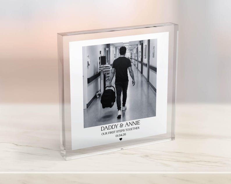 Puede incluir: Impresi&oacute;n fotogr&aacute;fica en blanco y negro en un bloque acr&iacute;lico transparente. La foto muestra a una persona caminando por un pasillo con un portabeb&eacute;s. El texto en la parte inferior dice "DADDY & ANNIE OUR FIRST STEPS TOGETHER 01.04.20" con un s&iacute;mbolo de coraz&oacute;n.