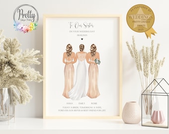 Puede incluir: Una impresión enmarcada con el texto "To Our Sister On Your Wedding Day 08.06.2023". La ilustración representa a tres mujeres con atuendo de boda. La impresión está en un marco de madera clara y presenta un sello dorado que dice "As Featured by Weddings".