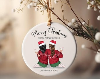 May include: White ceramic Christmas ornament with a red and green illustration of two friends wearing Santa hats and holding mugs. The text reads "Merry Christmas to my amazing friend" and "Shannon & Alice".