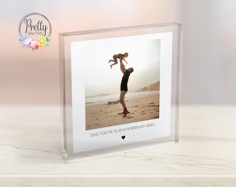 Puede incluir: Un bloque de foto de acrílico transparente con una foto de un padre y un hijo en una playa. El texto "DAD, YOU'VE ALWAYS BEEN MY HERO" está impreso debajo de la foto.