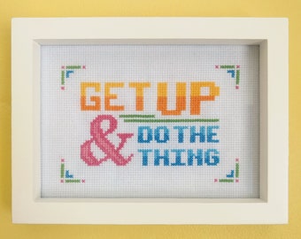 Puede incluir: Un bordado de punto de cruz enmarcado en blanco con el texto "GET UP & DO THE THING" en un esquema de colores arcoíris.
