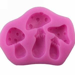 May include: Pink silicone mold with three mushroom shapes. The mold is designed to create edible mushroom decorations.