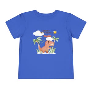 Puede incluir: Camiseta azul real para niños pequeños con un dinosaurio de dibujos animados y el texto "Happy Birthday Hayden". El diseño incluye un sol, nubes y palmeras. El dinosaurio es de color naranja claro.