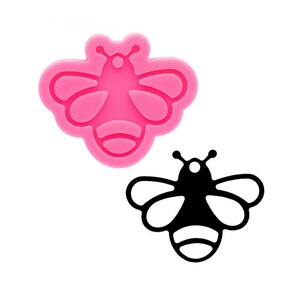May include: Pink silicone mold of a bee with black outline. The bee has a round body with wings and a stinger.