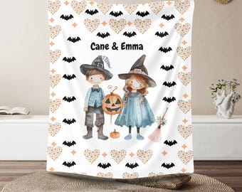 Könnte beinhalten: Weiße Halloween-Decke mit einem Jungen und einem Mädchen in Hexen- und Zaubererkostümen, mit dem Text "Cane & Emma". Die Decke hat ein sich wiederholendes Muster aus Fledermäusen, Herzen und Diamanten.