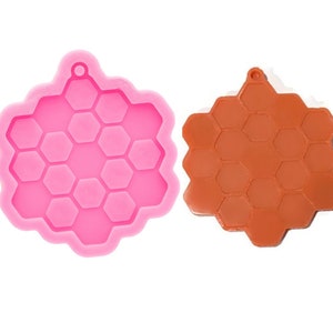 May include: A pink silicone mold shaped like a honeycomb, with a hole at the top for hanging. Next to it is a brown resin casting of the same honeycomb shape.