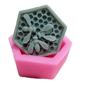 Może przedstawiać: Silikonowa forma sześciokątna z wzorem plastra miodu i trzema pszczołami. Forma jest r&oacute;żowa, a pszczoły są szare.