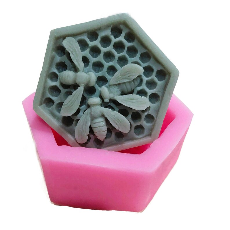 Może przedstawiać: Silikonowa forma sześciokątna z wzorem plastra miodu i trzema pszczołami. Forma jest r&oacute;żowa, a pszczoły są szare.