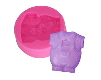 May include: A pink silicone mold in the shape of a baby's overall and a lavender overall. The mold is round with a cavity for the overall shape. The lavender overall is a solid, three-dimensional shape.