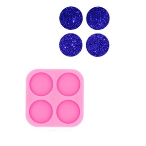 Puede incluir: Un molde de silicona rosa con cuatro cavidades redondas. Cuatro círculos de purpurina azul se muestran encima del molde.