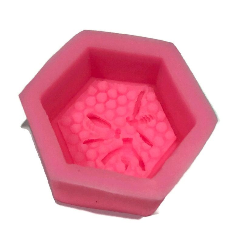 Może przedstawiać: R&oacute;żowa silikonowa forma w kształcie sześciokąta z wzorem plastra miodu i pszczoły w środku.