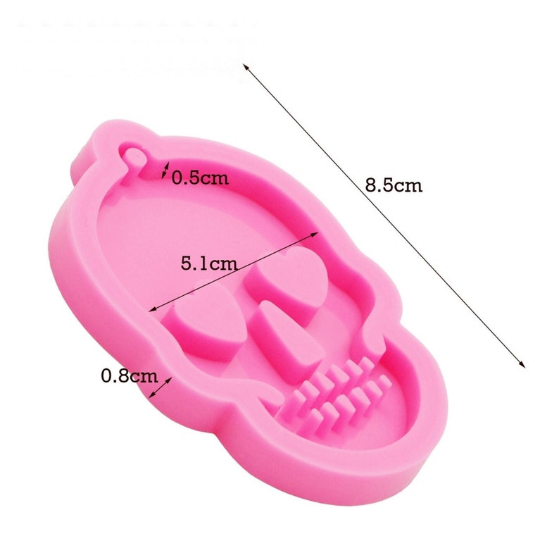 May include: Pink silicone skull mold with measurements: 8.5 cm x 5.1 cm x 0.8 cm. The mold has a hole at the top for hanging and a detailed skull design.