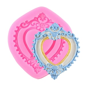 Puede incluir: Molde de silicona rosa con un diseño de marco en forma de corazón detallado. El molde se utiliza para crear una decoración de pastel en forma de corazón con un marco azul y dorado.