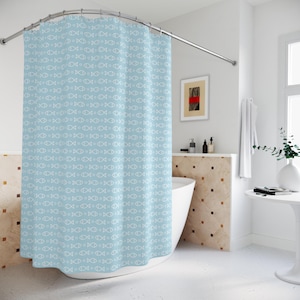 May include: A light blue shower curtain with a repeating pattern of white fish. The curtain is hanging from a curved, silver-colored shower rod. The bathroom has a white tub and a small table with a vase.