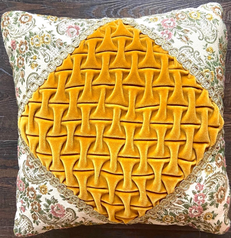 May include: Square decorative pillow with a floral patterned border and a central diamond-shaped design. The diamond is made of a textured, golden-yellow velvet fabric. The border features a cream-colored fabric with pink and yellow floral patterns.