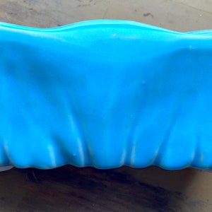 May include: A light blue ceramic planter with a wavy, ruffled edge. The planter is designed to look like a draped fabric.