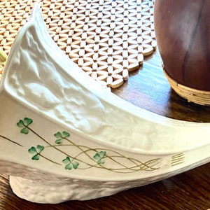 May include: A white ceramic cornucopia with green shamrock designs. The cornucopia is decorated with a Celtic knot design and has a textured surface.