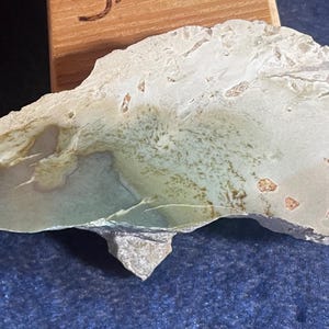 May include: A light green, white, and brown agate stone with a rough, natural texture. The stone has a unique, swirling pattern and is a beautiful example of natural beauty.