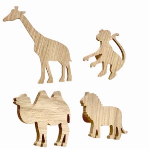 Könnte beinhalten: Vier Holzausschnitte von Tieren in Form einer Giraffe, eines Affen, eines Kamels und eines Löwen. Die Ausschnitte sind alle aus hellem braunem Holz gefertigt und haben eine natürliche Holzmaserung.