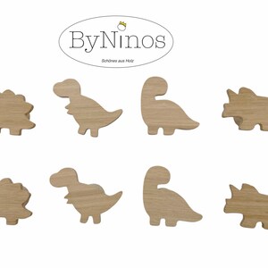Op de afbeelding: Set van acht houten haken in de vorm van dinosaurussen. De haken zijn in de vorm van een stegosaurus, tyrannosaurus rex, brachiosaurus en triceratops. De haken zijn allemaal van natuurlijke houtkleur.