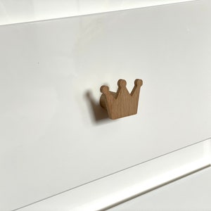 Könnte beinhalten: Ein brauner, kronenförmiger Schubladenknauf aus Holz.