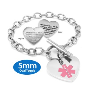 Op de afbeelding: Een zilveren medische ID-armband in de vorm van een hart met een 5 mm ovale sluiting. De armband heeft een lasergegraveerde boodschap met medische informatie, waaronder de naam "Janette Smith", medische aandoeningen en noodcontactgegevens. De armband heeft ook een roze ster-van-leven-symbool aan de andere kant.