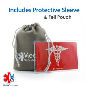 K&ouml;nnte beinhalten: Eine rote medizinische Notfallkarte mit einem silbernen Caduceus-Symbol und dem Text "MedicEngraved" ist in einer durchsichtigen Plastikh&uuml;lle zu sehen. Die Karte liegt auf einem grauen Filzbeutel mit Kordel.