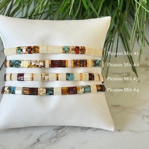May include: Four stacked bracelets with a white background. The bracelets are made of small, colorful square beads. The text "Picasso Mix #1", "Picasso Mix #2", "Picasso Mix #3", and "Picasso Mix #4" is written on the right side of the image.
