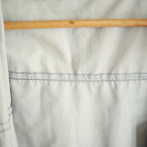 K&ouml;nnte beinhalten: Nahaufnahme des Innenraums einer hellfarbigen Jacke. Die Jacke h&auml;ngt an einem Holzb&uuml;gel. Der Innenstoff ist hellgrau mit einer horizontalen Naht aus grauen N&auml;hten. Die Oberseite der Jacke ist schwarz.