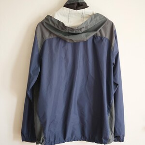 K&ouml;nnte beinhalten: Eine marineblaue und graue Kapuzenjacke h&auml;ngt an einer Wand. Die Jacke hat einen Kordelzug am unteren Saum und eine graue Kapuze. Die Oberseite der Jacke ist wei&szlig; und schwarz.