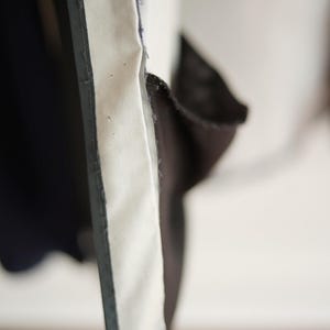 K&ouml;nnte beinhalten: Nahaufnahme eines Stoffabschnitts mit einem wei&szlig;en, strukturierten Panel, das von einer dunkelgrauen Umrandung begrenzt wird. Der Stoff scheint geschichtet zu sein, mit einem dunkelblauen Material auf der linken Seite.